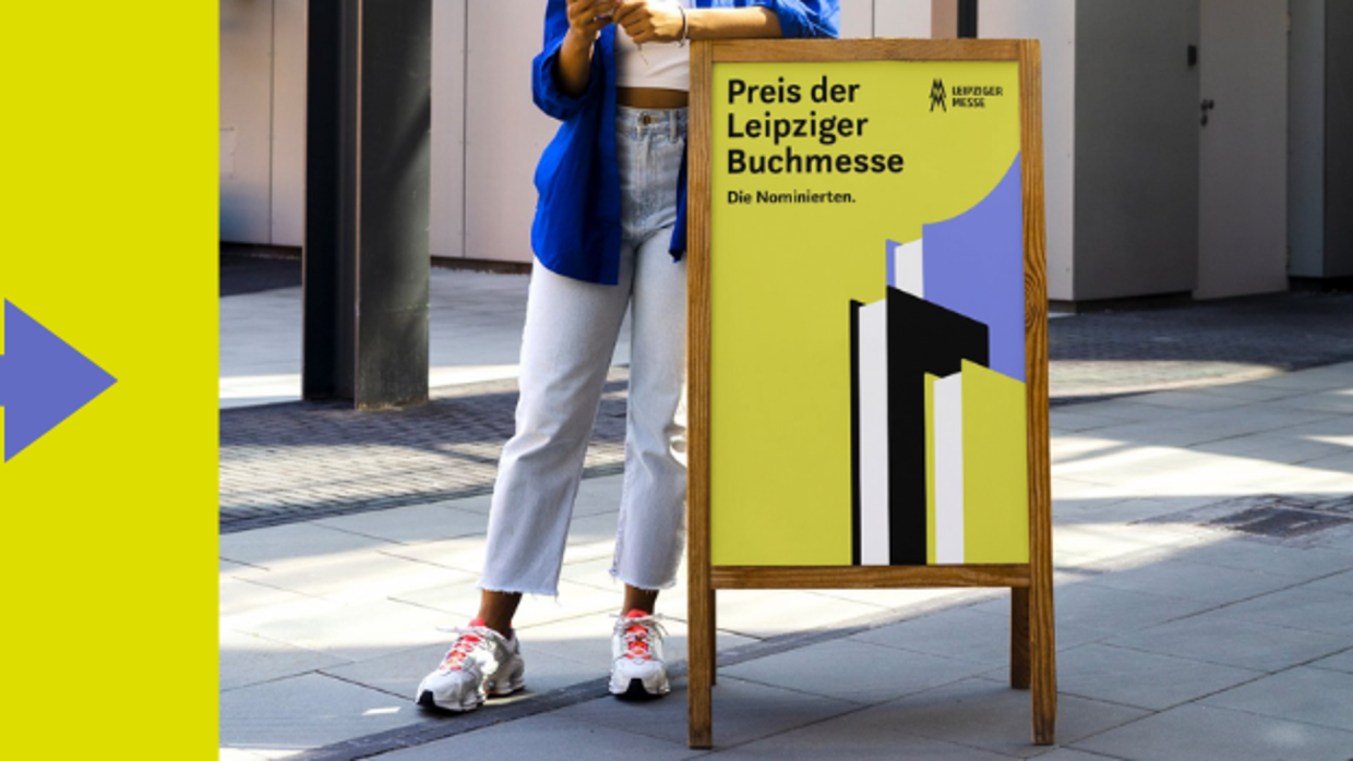 Weibliche Person lehnt an einem Plakataufsteller, der ein Plakat des Preises der Leipziger Buchmesse zeigt